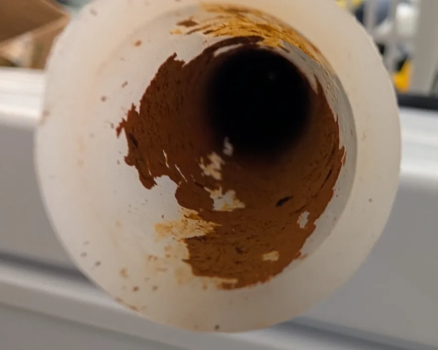 The cut end of a white PEX water pipe, stained orange-brown on the inside