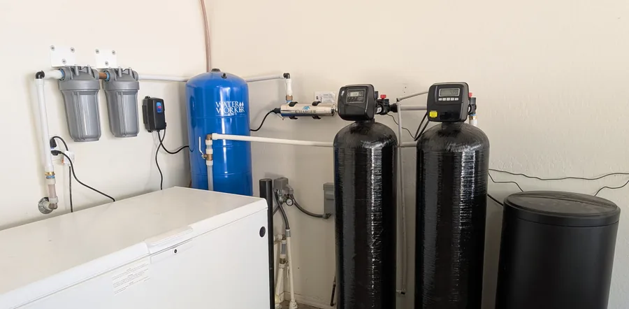 Two black 64,000-grain softener tanks with digital control valves and a large brine tank along a garage wall, with two filter housings and a blue pressure tank at the left