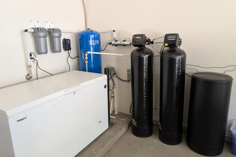 Whole-home water treatment installed by CreekWell in a Yavapai County garage: twin sediment and carbon pre-filters, pressure tank, UV sterilizer and two media tanks with a brine tank